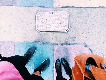 Low section of man and woman wearing black shoes standing on footpath