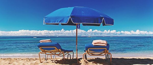 Deck chairs at beach against blue sky during sunny day