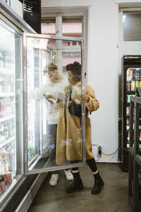 Full length of multiracial couple buying beverages from refrigerated section while doing shopping at supermarket