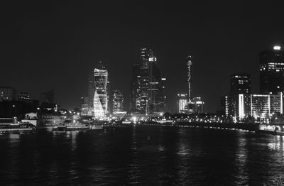 Illuminated city by sea against sky at night