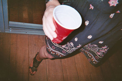 Low section of woman holding coffee cup on floor