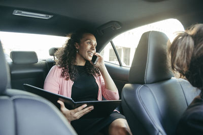 Businesswoman talking on smart phone while holding file in car