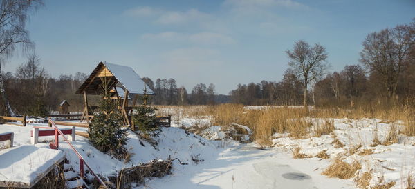 Built structure on snow covered field by houses against sky