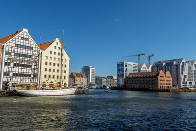 Sailboats in canal by buildings against blue sky