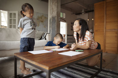 Girl talking to mother while brother drawing at table in living room