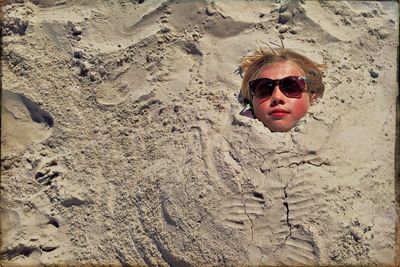 High angle view of teenage girl buried in sand at beach