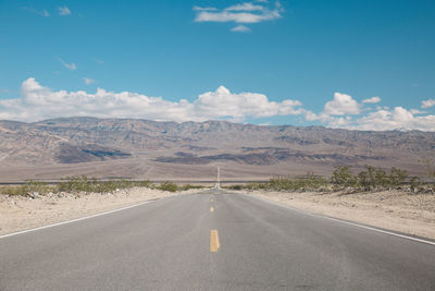 Empty road amidst field against sky