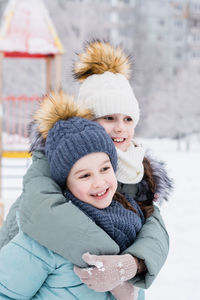 Two smiling girls in warm clothes are hugging in a snowy city. winter walks, lifestyle. 