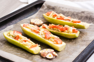 Raw zucchini halves, ready to bake, stuffed with cheese and tomato on baking paper on a baking sheet