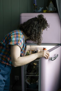 Side view of woman opening door of refrigerator in kitchen