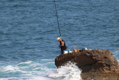 Man fishing on rock by sea