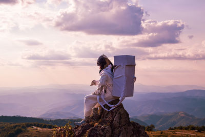 Rear view of an astronaut standing on mountain against sky during sunset