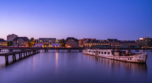 Illuminated bridge over river by buildings against sky at dusk