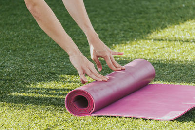 Cropped hands of woman folding exercise mat on grass