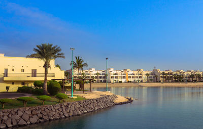 Buildings by palm trees against blue sky