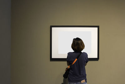 Rear view of woman standing against picture frame