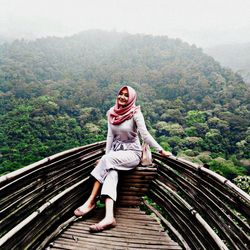 Portrait of young woman standing on mountain against trees