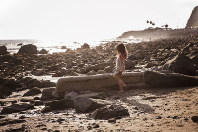Side view of girl standing at rocky beach during sunset