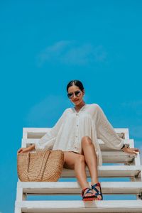 Portrait of young woman sitting on sunglasses against blue sky