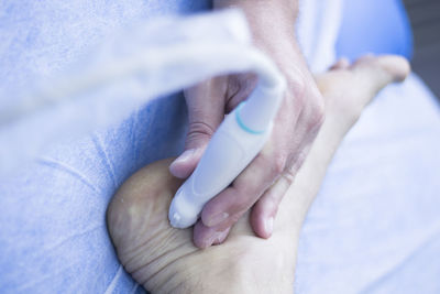 Cropped hands of doctor with medical equipment on patient on leg at hospital bed