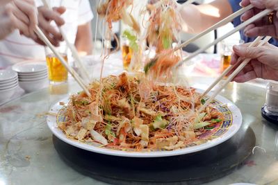 Cropped hands holding yusheng with chopsticks at home