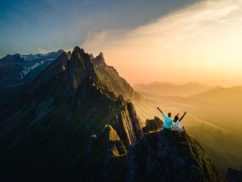 Panoramic view of people on rock against sky during sunset