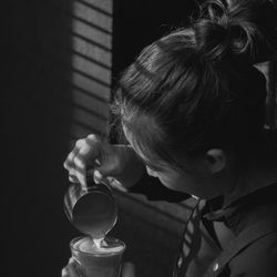 Side view of woman pouring coffee in cup at home