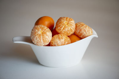 Peeling tangerines or clementines in white dish, isolated on white background