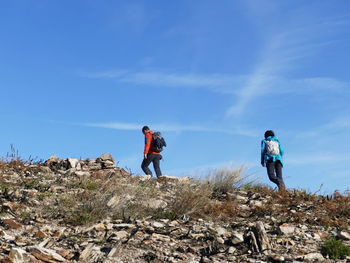 Low angle view of people walking on mountain against blue sky