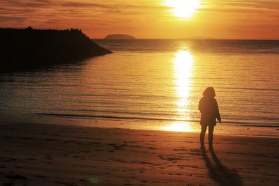 Silhouette woman standing at beach against sky during sunset