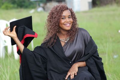 Portrait of smiling woman in graduation gown and mortarboard on field