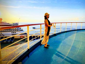 Man standing on railing against sea during sunset