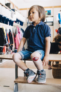 Full length of boy sitting on bench in cloakroom at preschool