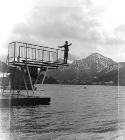 Man standing on pier by river with mountain in background