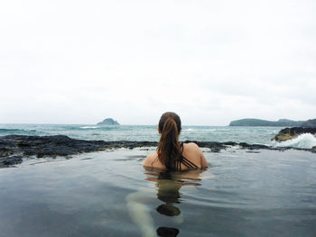 Rear view of woman in tidal pool looking at sea against sky