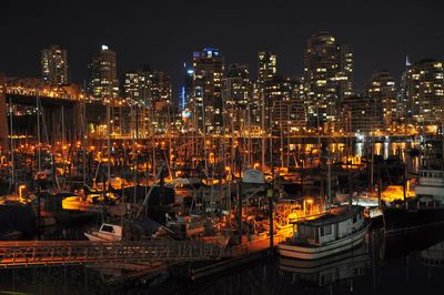 Illuminated sailboats moored at harbor by buildings at night