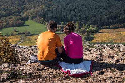 Rear view of couple sitting on cliff during sunny day