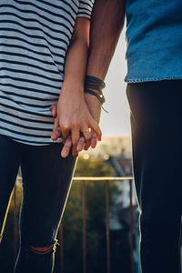 Midsection of couple holding hands against sky