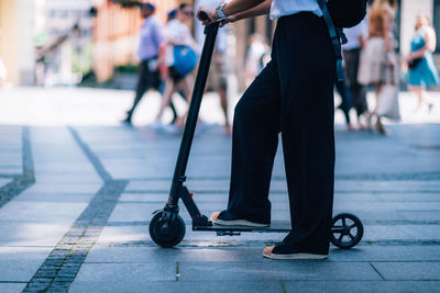 Low section of woman riding push scooter while standing on footpath