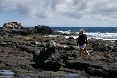 Rear view of woman on rock at beach against sky
