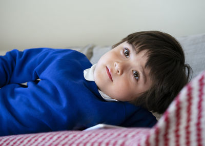 Portrait school kid lying on sofa watching tv, child laying down on couch relaxing in playroom 