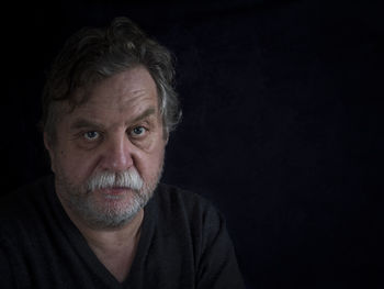 Close-up portrait of mature man against black background