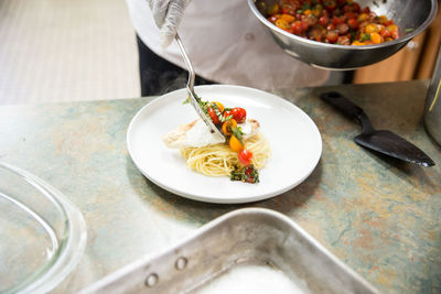 Cropped image of chef serving spaghetti in plate at table