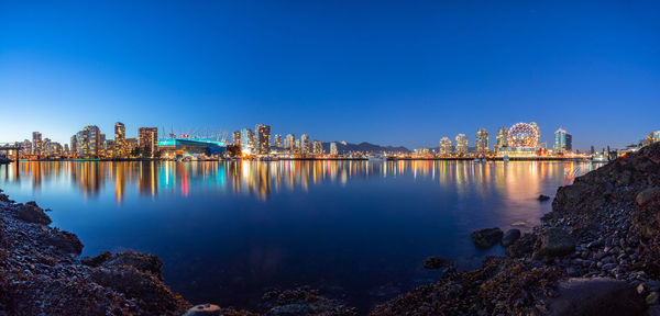 City buildings by river against clear blue sky during dusk