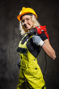 Smiling female worker looking away while holding drill against wall