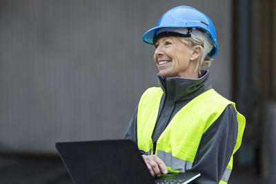 Happy mature female worker using laptop at factory