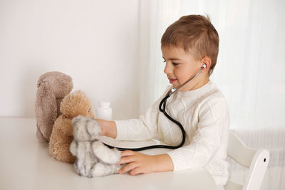 Cute little boy playing doctor at home and curing plush toy. sweet toddler child using stethoscope