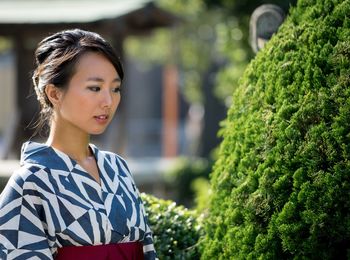 Young woman looking away while standing by plants