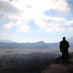 Rear view of man standing on mountain against sky