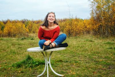 Portrait of young woman sitting on table against sky